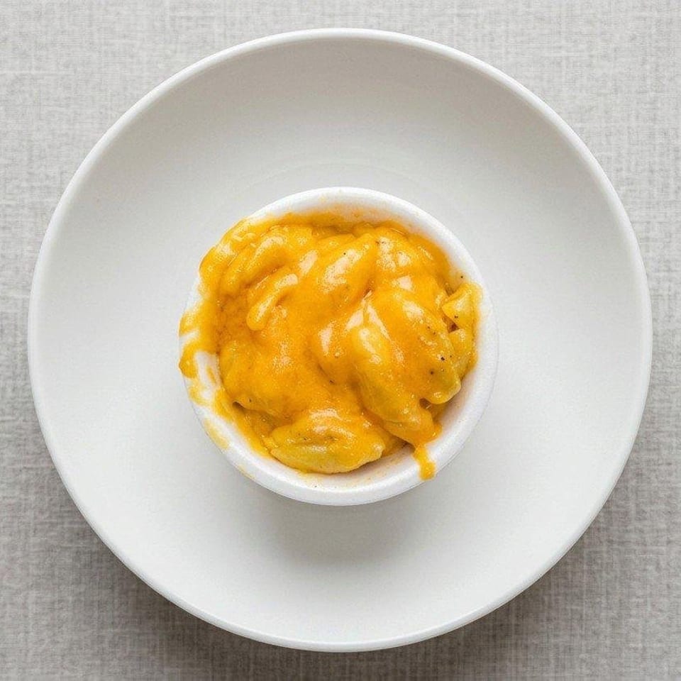 Overhead view of creamy orange pasta served in a small white bowl on a large white plate.
