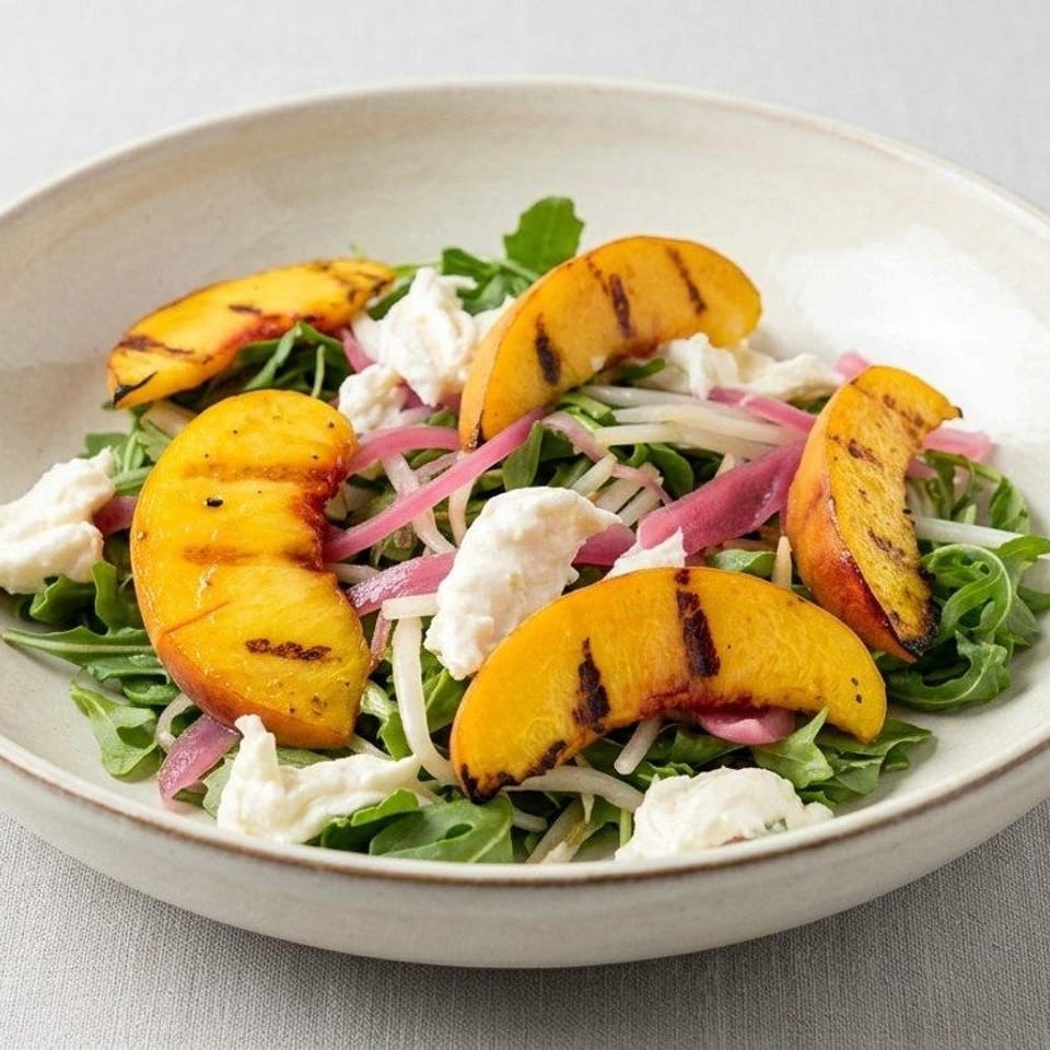 Arugula salad topped with grilled peach slices, creamy cheese, pickled onions, and shaved vegetables in a ceramic bowl.